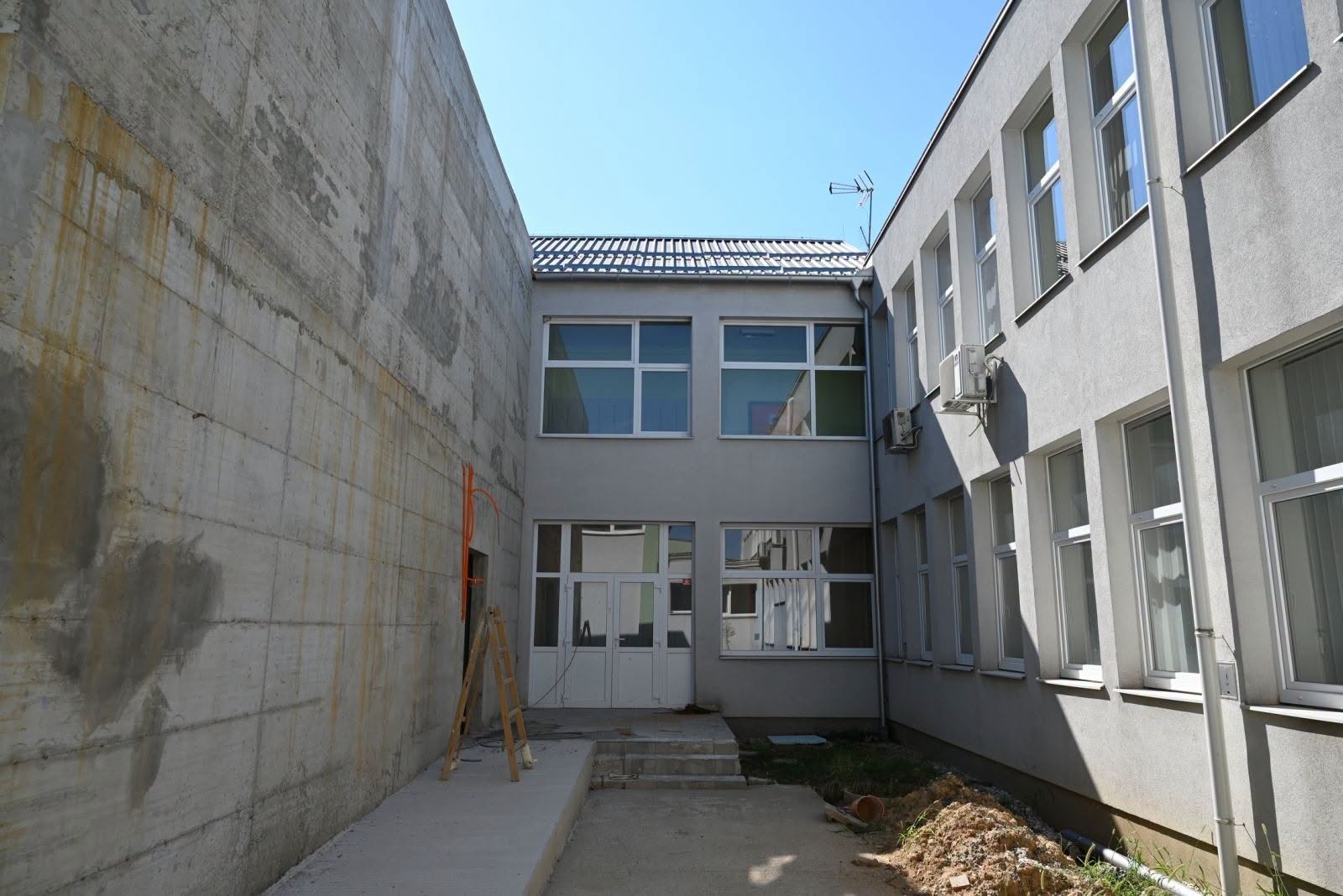 Pogled na dvorišni prostor zgrade s betonskim zidom i prozorima tijekom građevinskih radova.