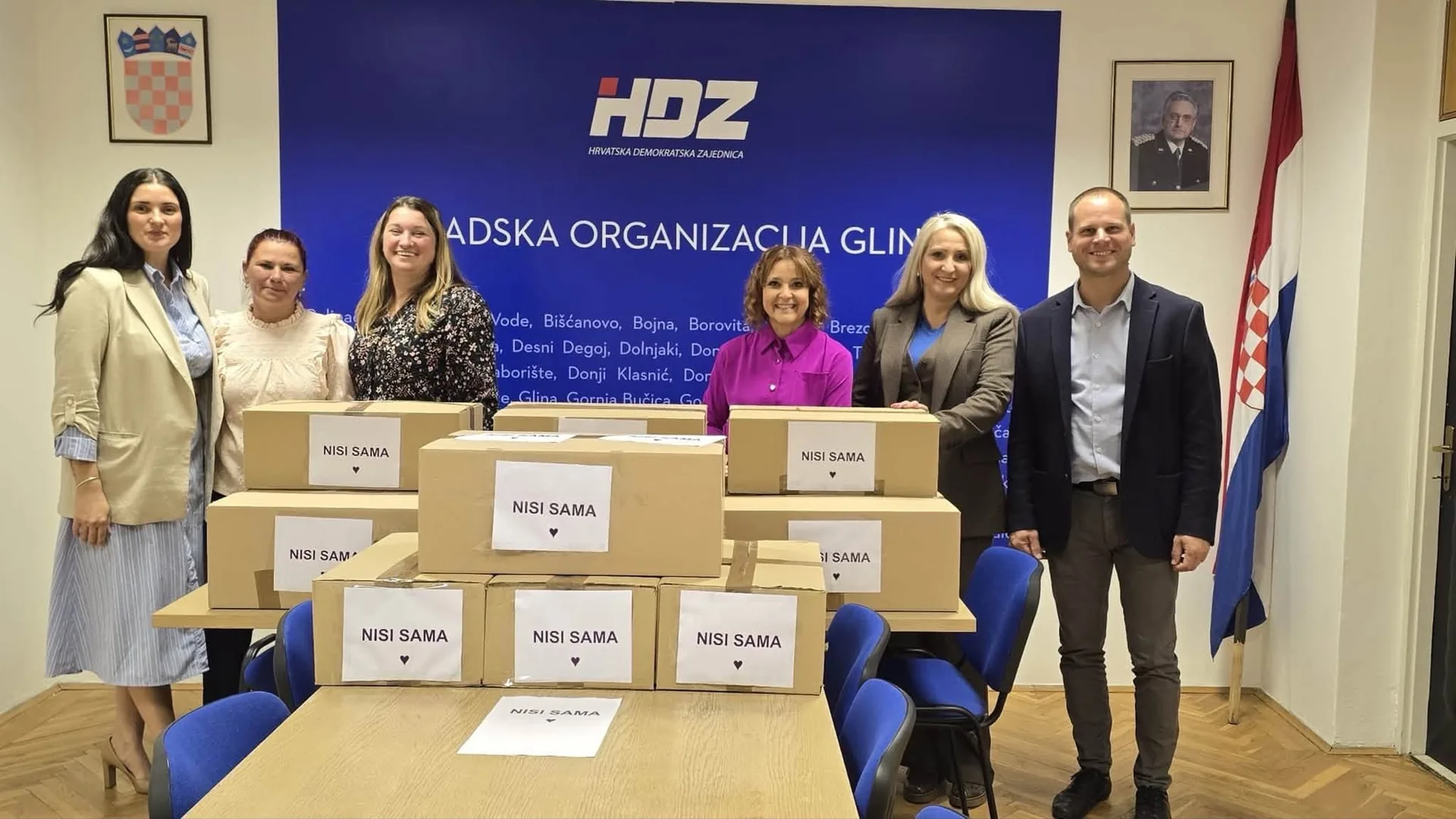 Šest osoba stoji iza naslaganih kutija s natpisom „Nisi sama“.
