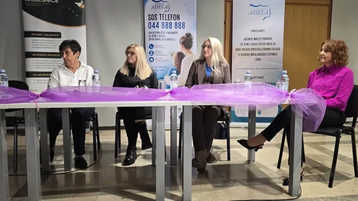 Četiri sudionice tribine sjede za stolom ispred panoa Centra za žene Adela.
